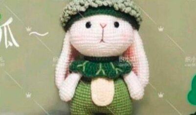 Мягкая вязаная игрушка-заяц с забавной шапкой-лягушкой и яркими градиентными ногами, идеально подходящая для уютных обниманий и украшения детской комнаты.